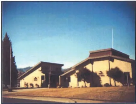 Exterior view of the Yreka City Hall and Council Chambers, two adjacent single-story buildings with angled rooflines and tan exterior walls, set against a clear sky with mountains in the background.