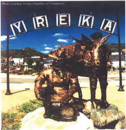 Bronze statue of a gold miner kneeling beside a pack mule beneath an arched sign spelling “YREKA,” serving as the gateway to Yreka’s Historic District. Mountains and the downtown area are visible in the background. Photo courtesy Yreka Chamber of Commerce.