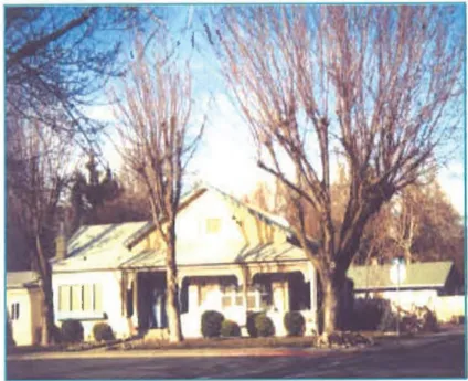 A historic single-story home with a covered front porch in an established Yreka neighborhood, framed by large bare deciduous trees in winter. The house features traditional architectural details and landscaped shrubs along the front.